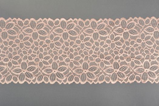 beige color straight strip of lace fabric on gray background. Elastic silk nylon braid border. use clothes linen decoration. repeating pattern and interweaving threads. texture for websites