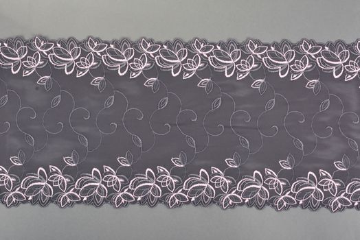 gray color straight strip of lace fabric on gray background. Elastic silk nylon braid border. use clothes linen decoration. repeating pattern and interweaving threads. texture for websites