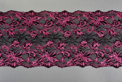 pink black color straight strip of lace fabric on gray background. Elastic silk nylon braid border. use clothes linen decoration. repeating pattern and interweaving threads. texture for websites