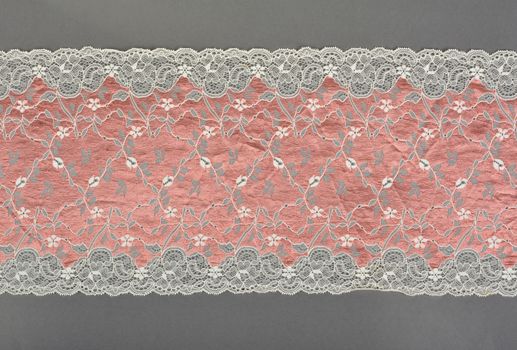 pink beige color straight strip of lace fabric on gray background. Elastic silk nylon braid border. use clothes linen decoration. repeating pattern and interweaving threads. texture for websites