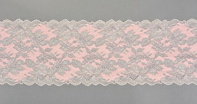 pink beige color straight strip of lace fabric on gray background. Elastic silk nylon braid border. use clothes linen decoration. repeating pattern and interweaving threads. texture for websites