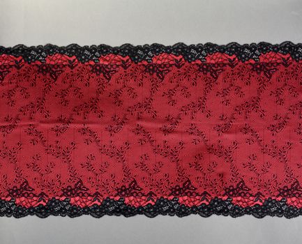 red black color straight strip of lace fabric on gray background. Elastic silk nylon braid border. use clothes linen decoration. repeating pattern and interweaving threads. texture for websites