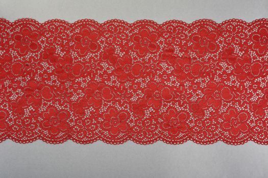 red color straight strip of lace fabric on gray background. Elastic silk nylon braid border. use clothes linen decoration. repeating pattern and interweaving threads. texture for websites