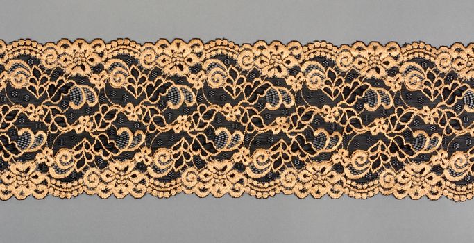 gold, black color straight strip of lace fabric on gray background. Elastic silk nylon braid border. use clothes linen decoration. repeating pattern and interweaving threads. texture for websites