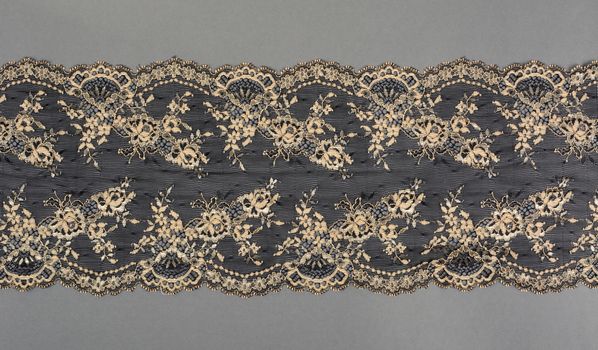 black beige color straight strip of lace fabric on gray background. Elastic silk nylon braid border. use clothes linen decoration. repeating pattern and interweaving threads. texture for websites
