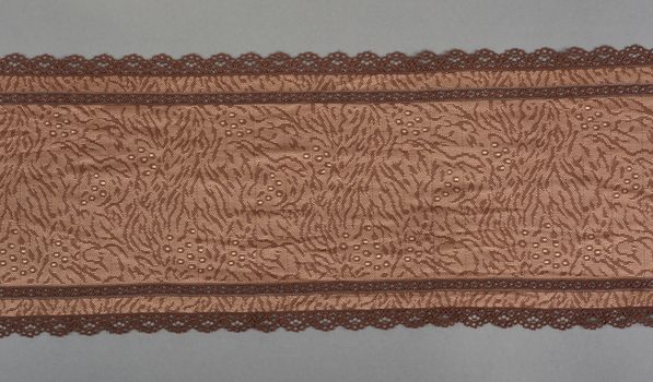 brown beige color straight strip of lace fabric on gray background. Elastic silk nylon braid border. use clothes linen decoration. repeating pattern and interweaving threads. texture for websites