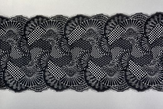 black gray color straight strip of lace fabric on gray background. Elastic silk nylon braid border. use clothes linen decoration. repeating pattern and interweaving threads. texture for websites