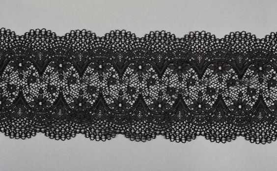 black gray color straight strip of lace fabric on gray background. Elastic silk nylon braid border. use clothes linen decoration. repeating pattern and interweaving threads. texture for websites