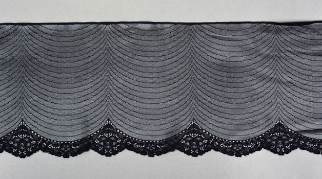 black gray color straight strip of lace fabric on gray background. Elastic silk nylon braid border. use clothes linen decoration. repeating pattern and interweaving threads. texture for websites