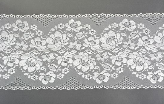 white color straight strip of lace fabric on gray background. Elastic silk nylon braid border. use clothes linen decoration. repeating pattern and interweaving threads. texture for websites