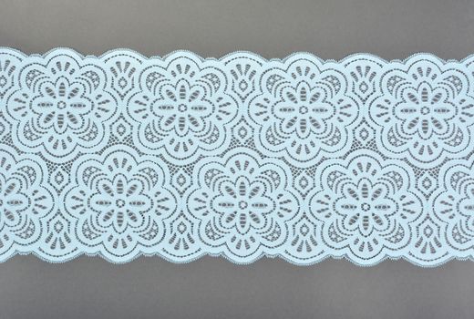 blue color straight strip of lace fabric on gray background. Elastic silk nylon braid border. use clothes linen decoration. repeating pattern and interweaving threads. texture for websites