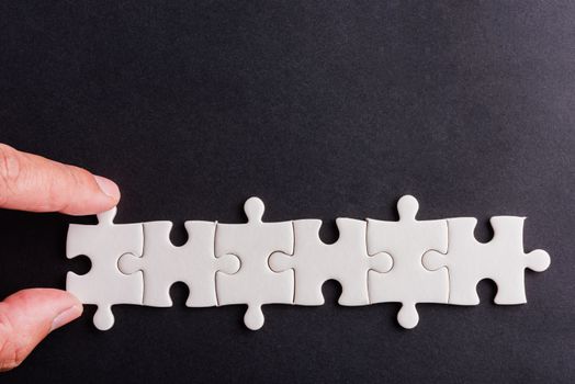 Top view flat lay of hand-holding last six-piece white paper jigsaw puzzle game last pieces for solve problem, studio shot on a black background, quiz calculation concept