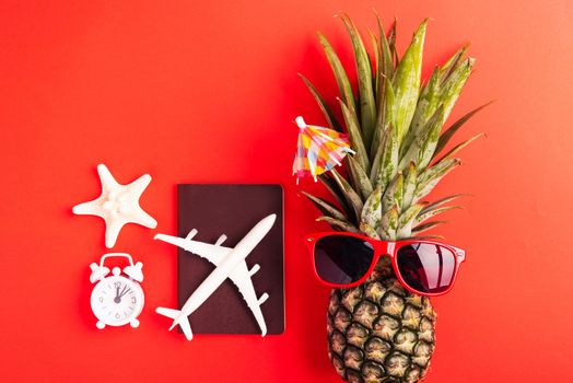 Summer Pineapple Day Concept, Top view flat lay of funny pineapple wear red sunglasses, model plane, starfish, passport and clock alarm isolated on red background, Holiday summertime in tropical