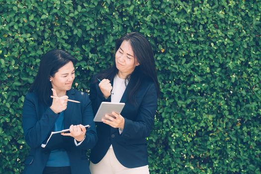 Two business people discussing information on a tablet-and taking notes as they work together as a team in the garden.