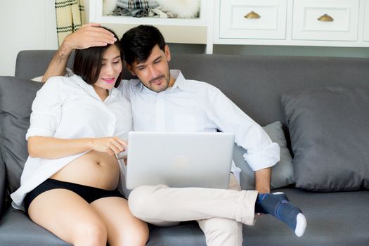 Portrait of a asian young couple husband and wife sitting on the sofa while using notebook computer in living room.