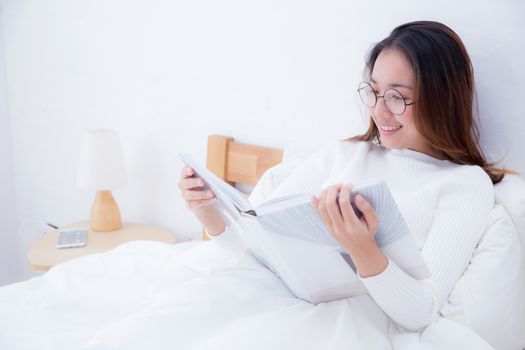 Asian woman reading a book and smiling in bedroom. lifestyle concept.