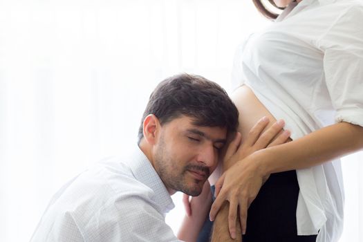 Asian man father ear listening to the belly of the pregnant wife to the movements of the child.