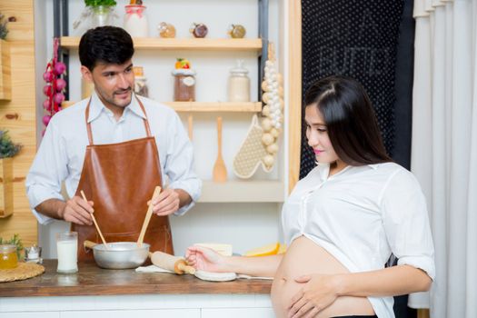 Happy husband and pregnant wife in kitchen,Asian man cooking food in kitchen at home,Happy family concept.