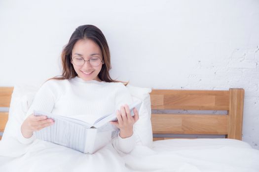 Asian woman reading a book and smiling in bedroom. lifestyle concept.