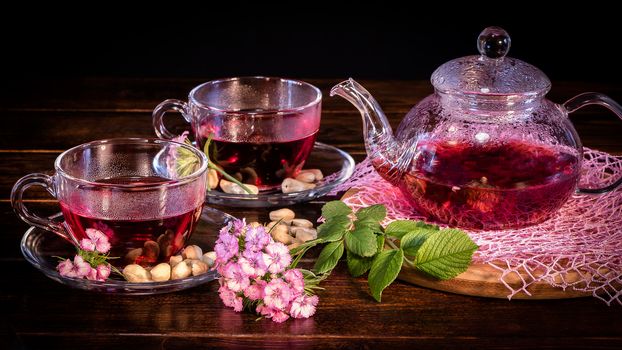 Tea parties, tea traditions and ceremonies. Zen traditions of the East.Green tea leaves or leaves of medicinal herbs lie on the table with a teapot and mugs of red tea, cashew nuts and clove flowers