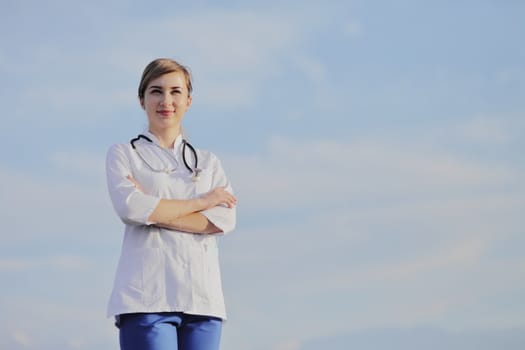 Portrait of a beautiful female doctor or nurse against blue sky with clouds. Prevention Covid-19 healthcare concept. Stethoscope over the neck. Woman, girl.