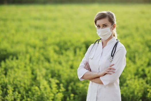 Female doctor or nurse wearing a protective face mask on green grass background. Safety measures against the coronavirus. Prevention Covid-19 healthcare concept. Stethoscope over the neck. Woman, girl