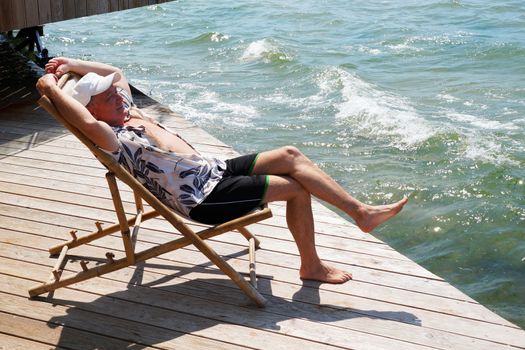 smiling man resting on a sun lounger on the patio near the sea