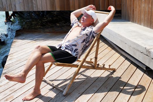 smiling man resting on a sun lounger on the patio near the sea