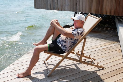 smiling man resting on a sun lounger on the patio near the sea