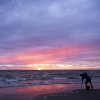 man on normandy beach during colorful sunset looks for worms to use as bait for fishing