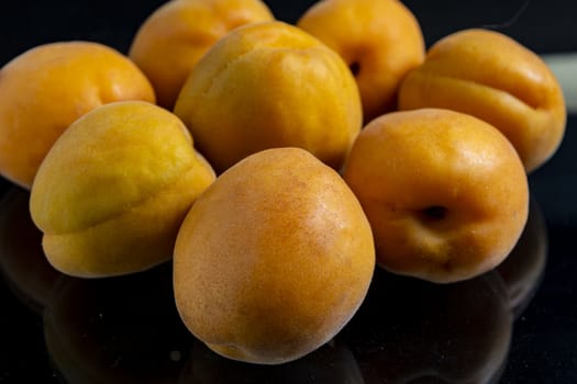 A pile of scattered apricots lie with reflection on a black glass