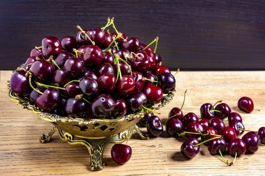 Cherries in a bronze vase on a wooden table against a black background