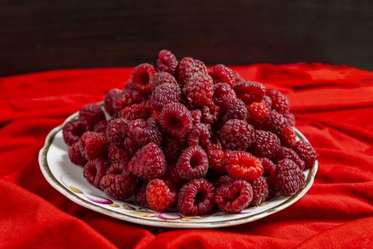 Raspberry berry lies on a plate on a red tablecloth