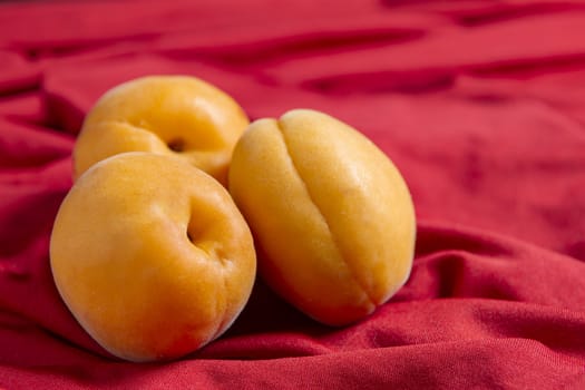 Three apricots lie on a red tablecloth against a red background