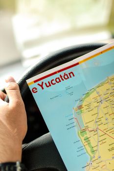 Man driving car checking map of Yucatan, Mexico during his summer holiday trip