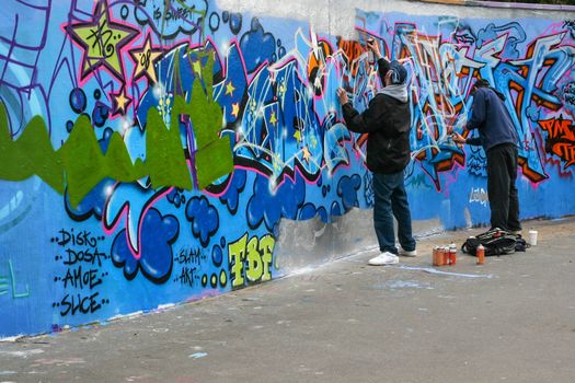 London, United Kingdom - April 20th, 2008: Two boys spraying graffiti on concrete wall during day