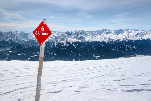 Red ski route 6 sign on fresh snow with Austrian Alps and sky in background photographed in Nordpark, Innsbruck