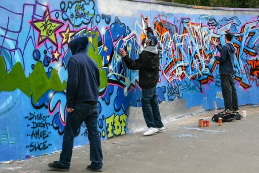 London, United Kingdom - April 20th, 2008: Three boys painting graffiti with sprays on concrete wall during day