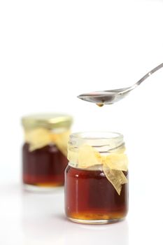 honey dripping from spoon on top of jar, isolated on white background 