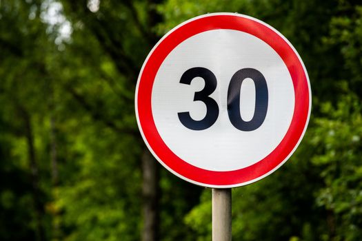 Road sign speed limit 30 kilometers per hour on green forest background with selective focus. End of youth symbol too. Horizontal orientation.