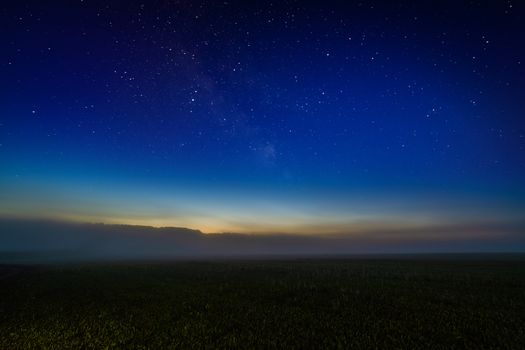 Foggy night field with starry night sky and afterglow horizon gradient. Collage.