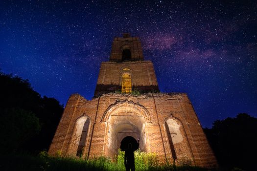 night bell tower ruin in forest at starry night and man with flashlight under it.