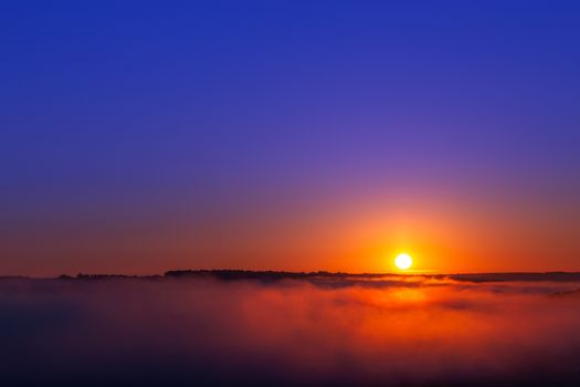 golden-blue summer sunrise over fog without clouds in minimalistic composition.