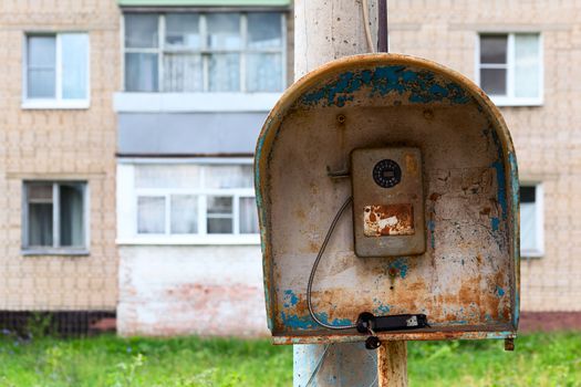 Old public russian wired urban telephone post - useless abandoned and broken. Horizontal shot with selective focus and blurred suburbs condominium house in background.