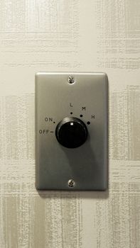 Air condition controls button on the wall made from black color plastic material and clean texture wallpaper.