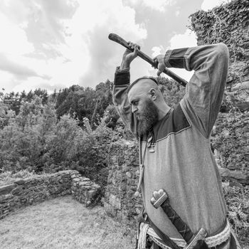 A man in medieval clothes wields an ax in the ruins of an ancient castle, a Viking historical reenactment