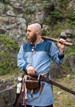 A man in medieval clothes wields an ax in the ruins of an ancient castle, a Viking historical reenactment