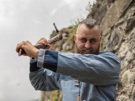 A man in medieval clothes wields an ax in the ruins of an ancient castle, a Viking historical reenactment