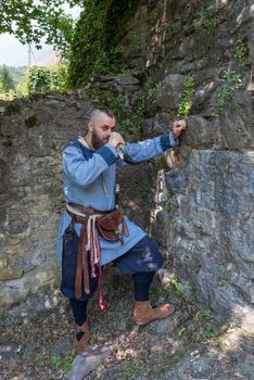 A Viking warrior drinks cider from a horn leaning against a stone wall, image of man in medieval clothes