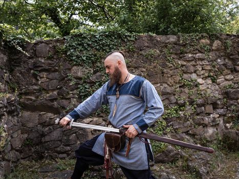 Medieval warrior draws sword from scabbard, Viking in traditional clothing